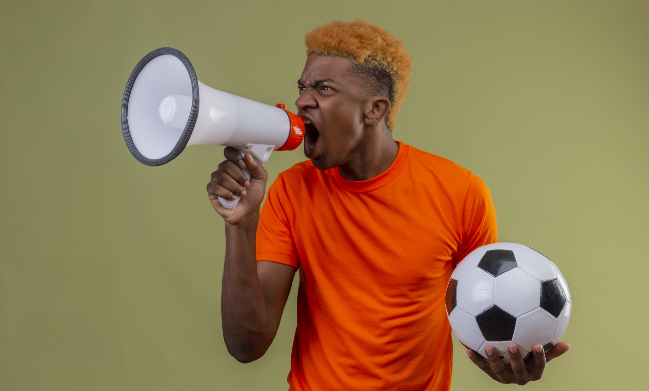young-boy-wearing-orange-t-shirt-holding-soccer-ball-shouting-megaphone-with-angry-expression-face-standing-green-wall